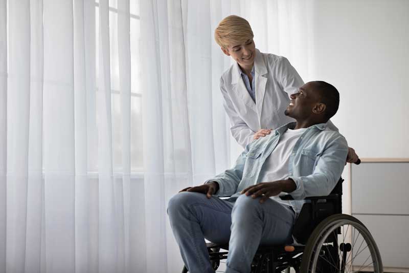 Homme docteur qui parle en souriant à un patient en fauteuil roulant